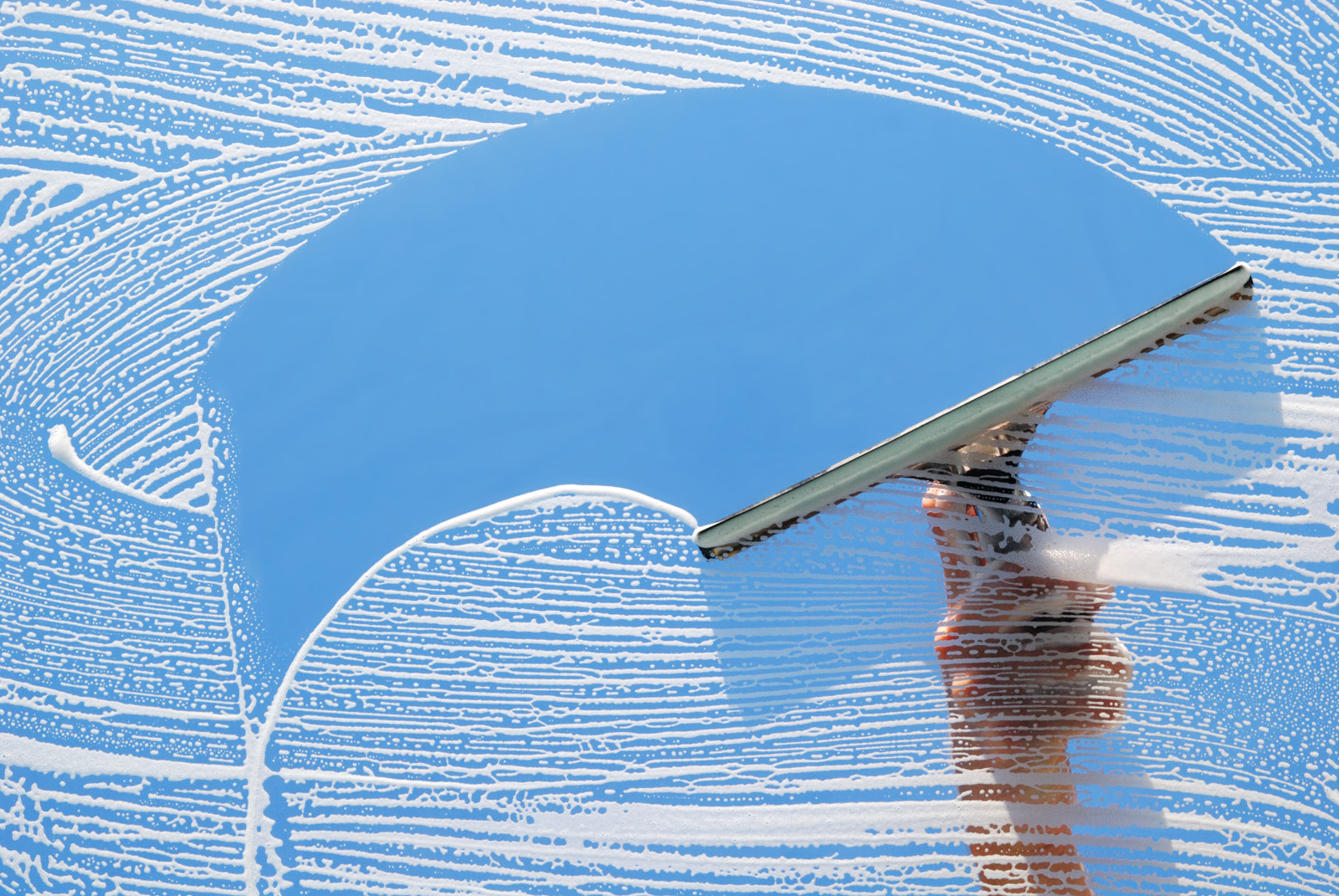Close-up of hand squeegee cleaning soapy window glass